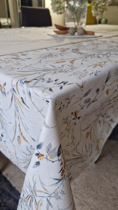 Mantel rectangular Sofía repelente puesto sobre mesa, con estampado de ramas y pajaritos sobre fondo blanco y caída por el borde