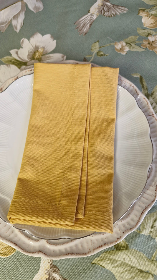 Servilleta repelente color mostaza doblada sobre un plato blanco de loza