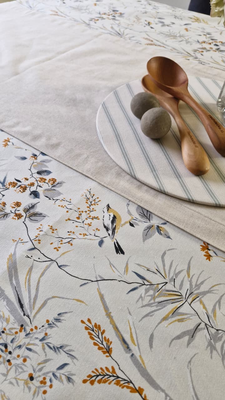 Detalle del estampado Sofía: pajarito posado en una rama con bayas naranjas y hojas azul grisáceo sobre lona turca blanca