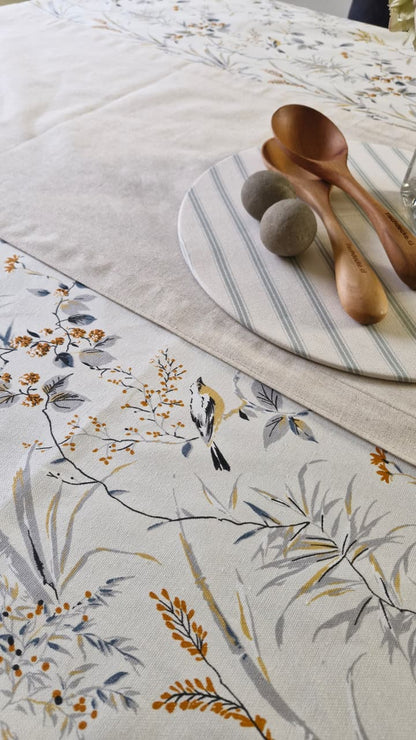Detalle del estampado Sofía: pajarito posado en una rama con bayas naranjas y hojas azul grisáceo sobre lona turca blanca