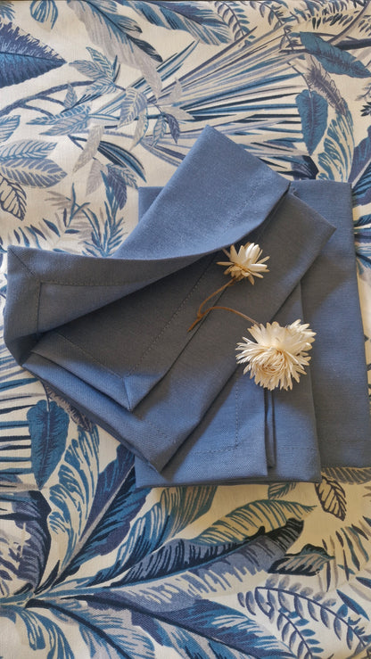 Las cuatro servilletas azul piedra apiladas sobre mantel de hojas azules, con flores secas