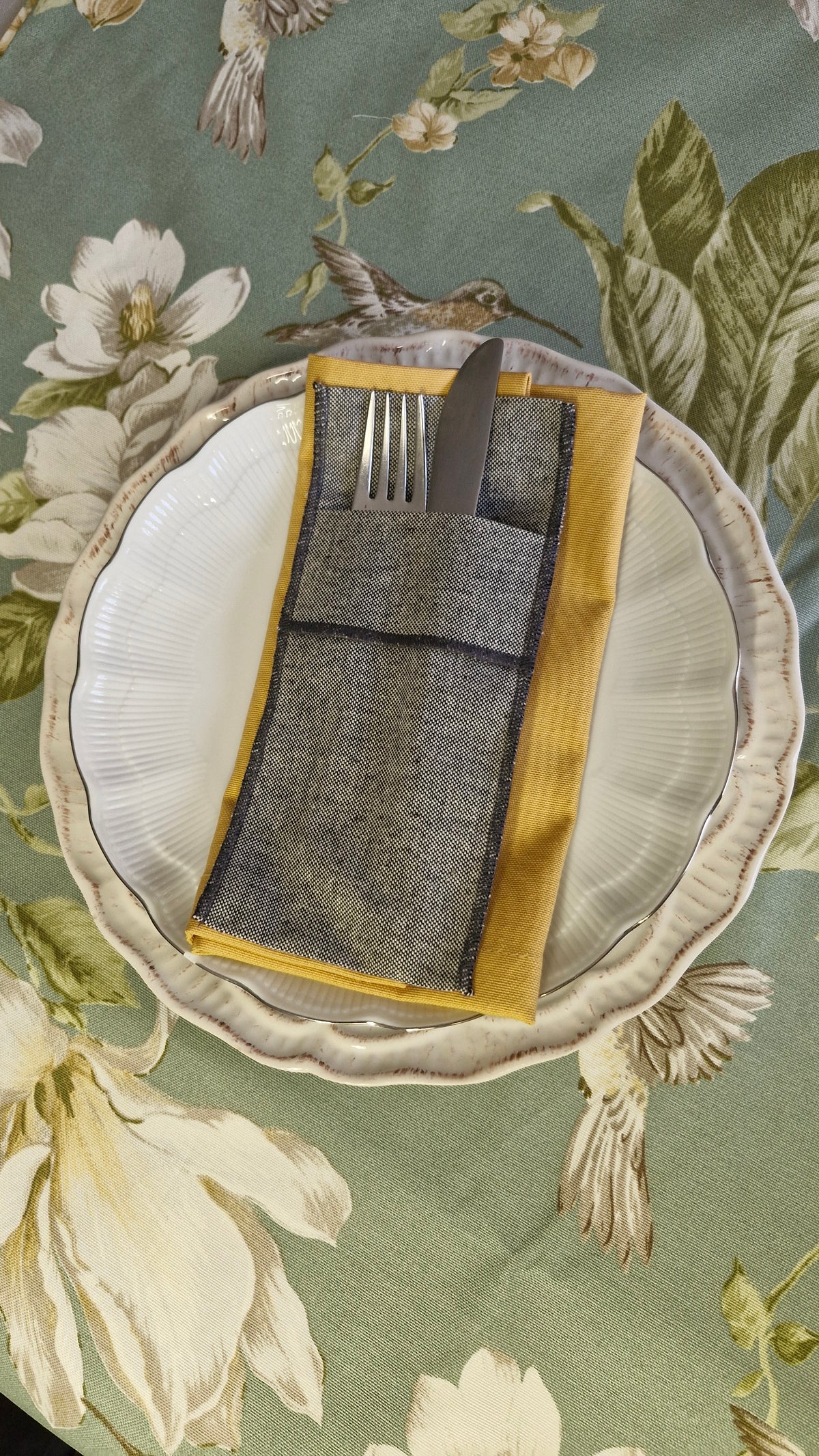 Vista cenital de la mesa puesta con servilleta repelente mostaza, plato blanco y cubiertos