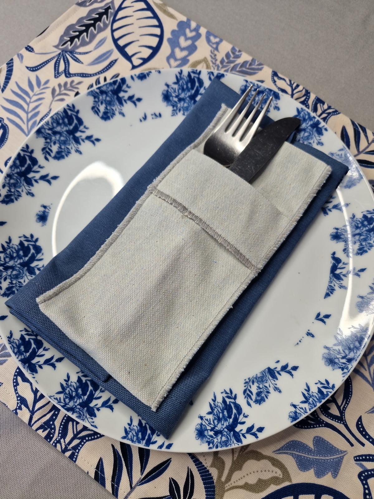 Puesto de mesa con servilleta azul piedra, funda de cubiertos en lino y plato azul y blanco
